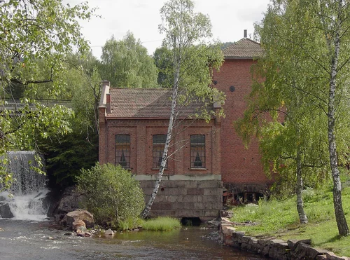 Den gamle kraftstasjonen i rød teglstein ved Brekkefossen, omkranset av bjørketrær en sommerdag